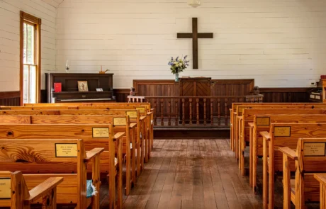 Interior of a historic wooden church with white walls, wooden pews, altar, and cross