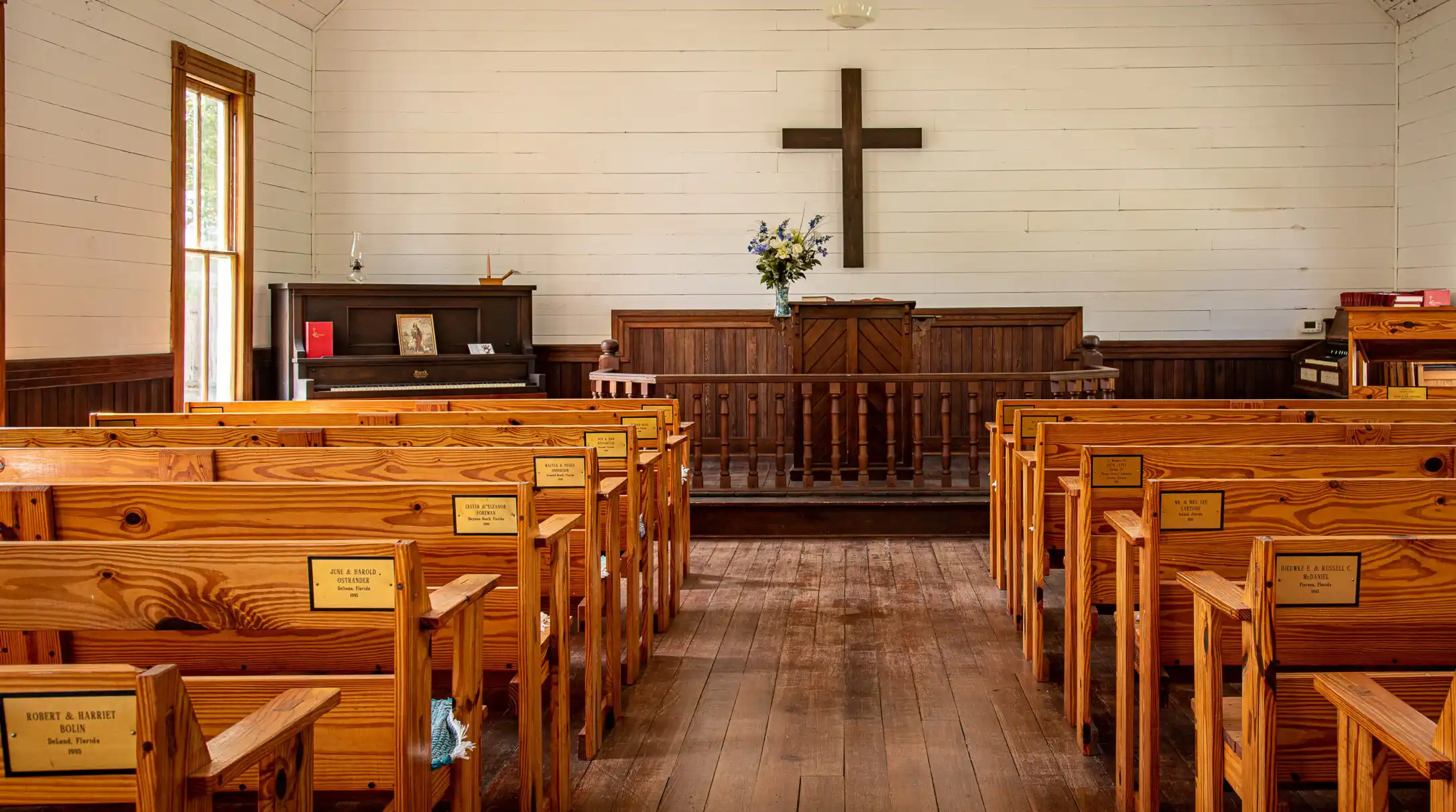 Interior of a historic wooden church with white walls, wooden pews, altar, and cross