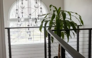 Modern loft with black cable railing, hanging pendant lights, and potted plant