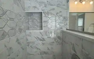 Walk-in shower with grey and white marble subway tile, geometric accent band, built-in niche, and chrome fixtures