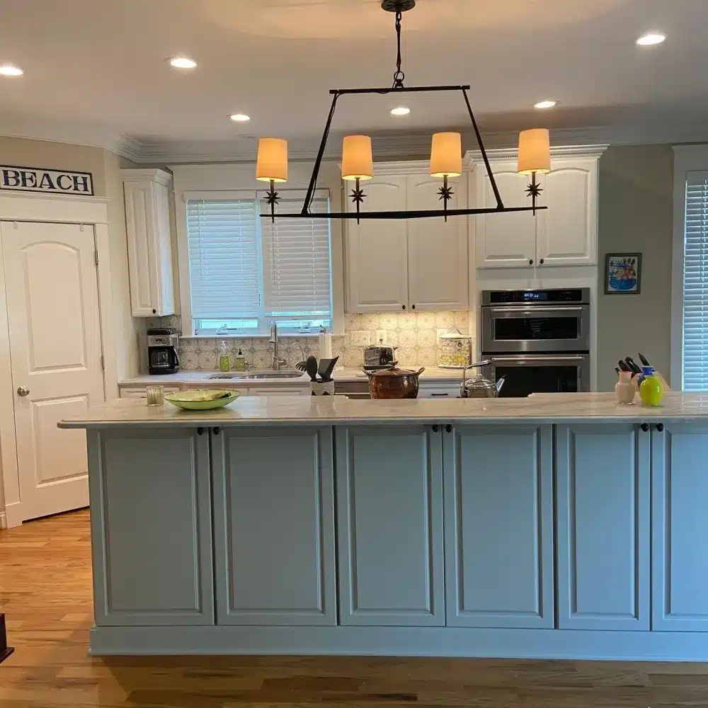 Light grey kitchen island and white cabinets with a metal chandelier