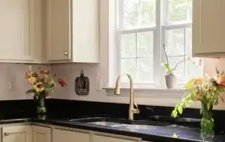 Freshly painted light beige kitchen cabinets with gold hardware and black countertops