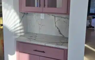 Built-in pink painted kitchen cabinets with glass doors and marble backsplash