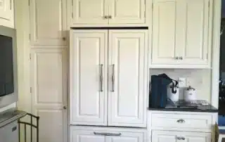 White kitchen cabinets surrounding a built-in refrigerator with custom paneling