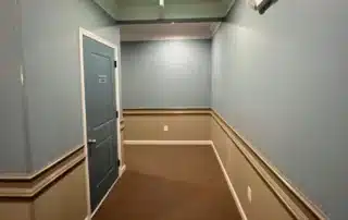 Commercial hallway with blue and beige walls, white wainscoting, and a blue door