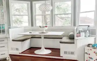 Raised wooden kitchen banquette seating and dining table in a bay window
