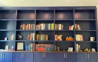 Navy blue built-in bookshelf with beadboard backing and lower storage cabinets