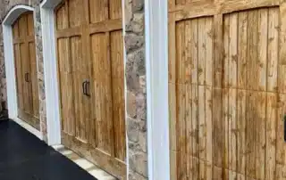 Three custom wooden arched garage doors installed on a stone exterior wall