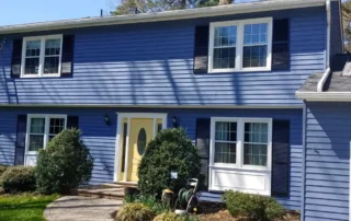 Two-story blue house with white trim, black shutters, and a yellow front door