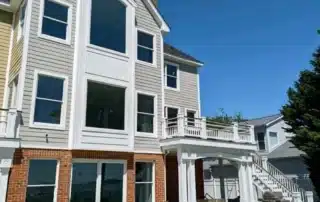 Multi-story residential home exterior with grey siding, brick foundation, and patio deck in Annapolis MD