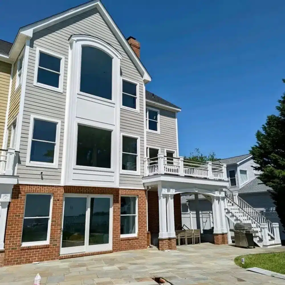 Multi-story residential home exterior with grey siding, brick foundation, and patio deck in Annapolis MD