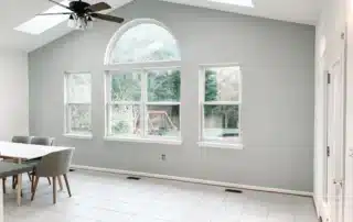 Bright dining room interior with light grey walls, large arched windows, and white tiled floor