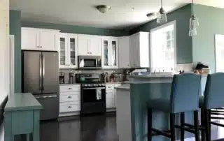 Modern kitchen with blue walls, white upper cabinets, stainless steel appliances, and bar stools at peninsula