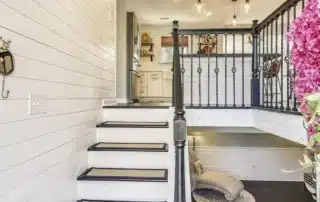 Stairs with white risers, black handrails, and patterned runners leading to a kitchen