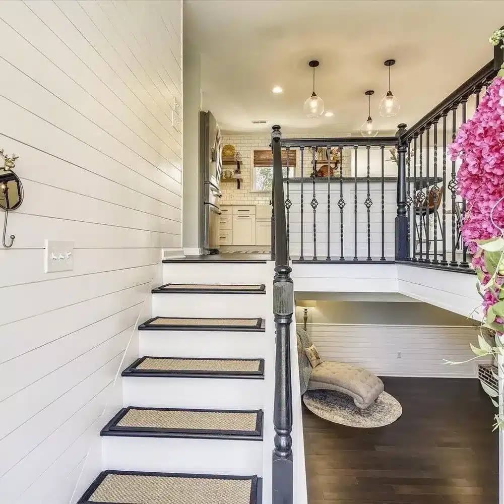 Stairs with white risers, black handrails, and patterned runners leading to a kitchen