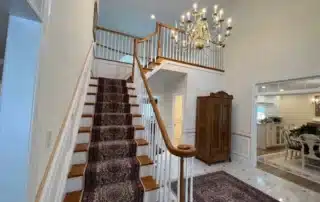 Grand foyer with carpeted staircase, white railing, and decorative chandelier