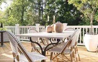 Patio dining table with woven chairs on a wooden deck overlooking trees