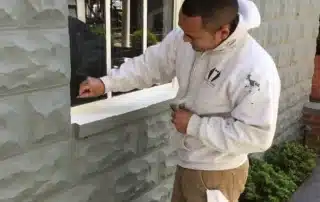 Worker in white hoodie cleaning window exterior of stone building