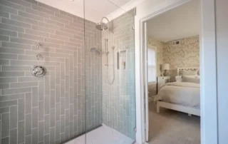Glass shower enclosure with grey subway tile and open view into a bedroom