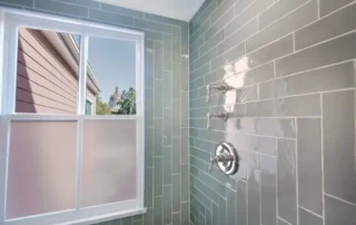 Modern bathroom shower with green subway tile and chrome fixtures next to a window