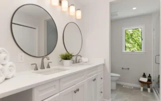 White double vanity with round mirrors and modern light fixture in a bright bathroom
