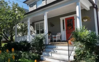 Grey residential house exterior with white trim and a bright orange front door