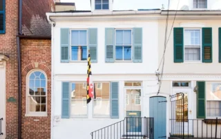 White historic townhome in Annapolis with blue shutters and a Maryland flag