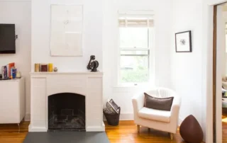 Interior Painting White Brick Fireplace Annapolis Md Bright white painted living room walls with a white brick fireplace, hardwood floors, and a white armchair