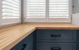 Blue kitchen cabinets with butcher block wood countertops and white shutters
