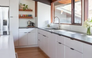 Modern residential kitchen with white cabinets, dark countertops, and large windows