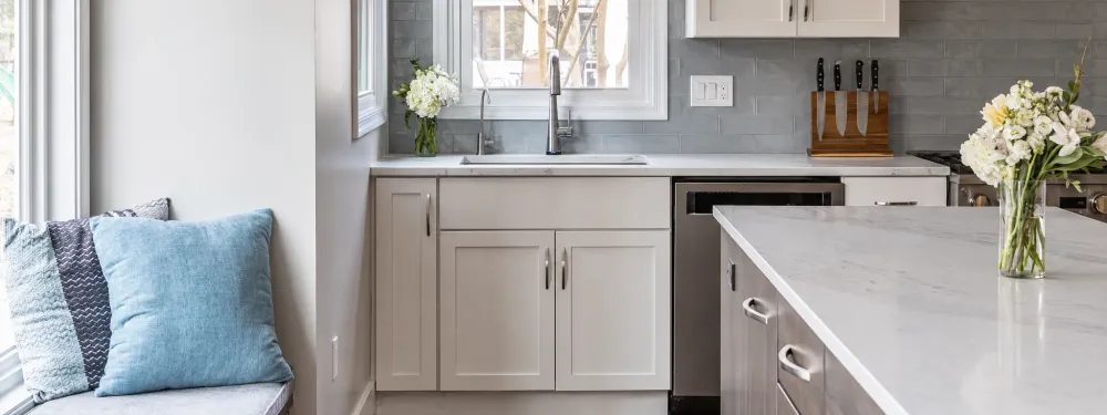 Modern kitchen with white cabinets, marble countertops, and a window seat