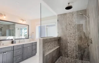 Modern bathroom featuring a grey double vanity, white countertop, large mirror, and a walk-in shower with grey stone tiles an