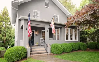 Grey painted two-story home with white trim, porch, and manicured green bushes