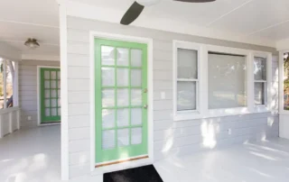 Freshly painted grey siding and white trim on a home porch with a green screen door