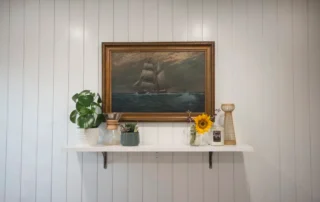 Residential Interior Painting White Shiplap Shelf Annapolis Md White vertical panel wall with a floating wooden shelf holding potted plants and framed ship painting