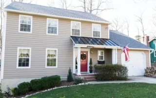 Tan two-story residential house with white trim, dark roof over porch, and attached garage