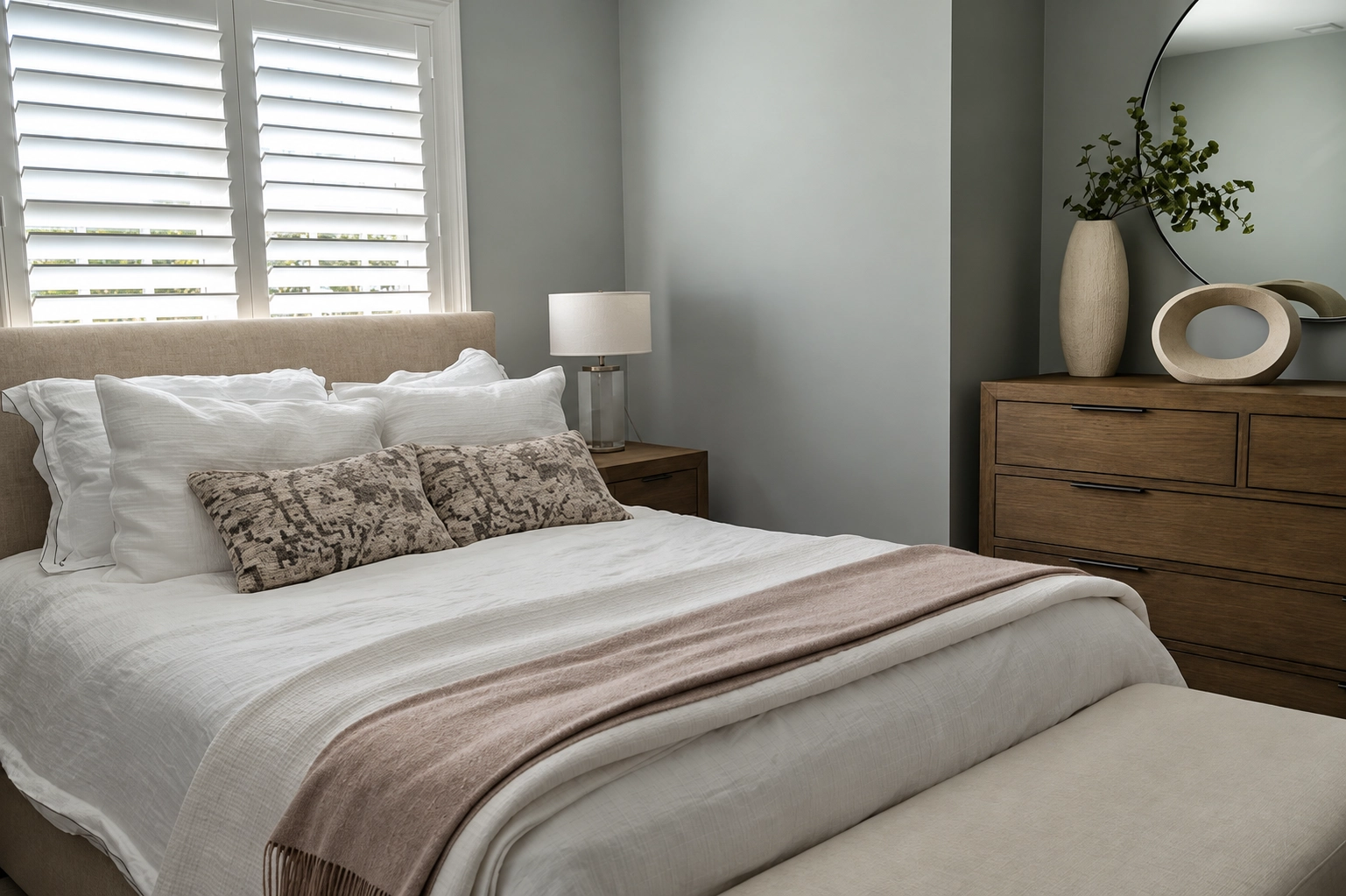Neutral bedroom with white bedding, window shutters, and a wood dresser