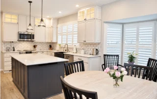 White kitchen with a dark island, window shutters, and an adjacent dining table