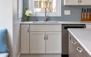 White kitchen cabinets beneath a window with a gray subway tile backsplash