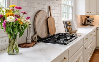 White kitchen cabinets with brass hardware, a gas cooktop, and marble backsplash